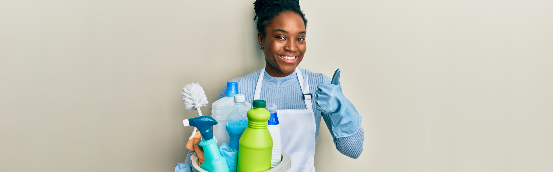 woman with braided hair wearing apron holding cleaning products